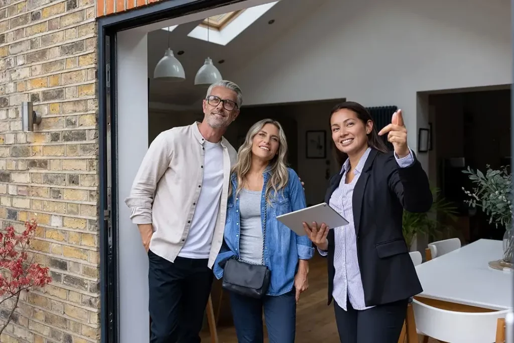 A homeowner couple and businessperson looking outside and smiling while businessperson points at something.