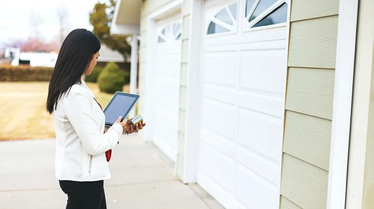 Businessperson holding tablet standing in front of two car residential garage.