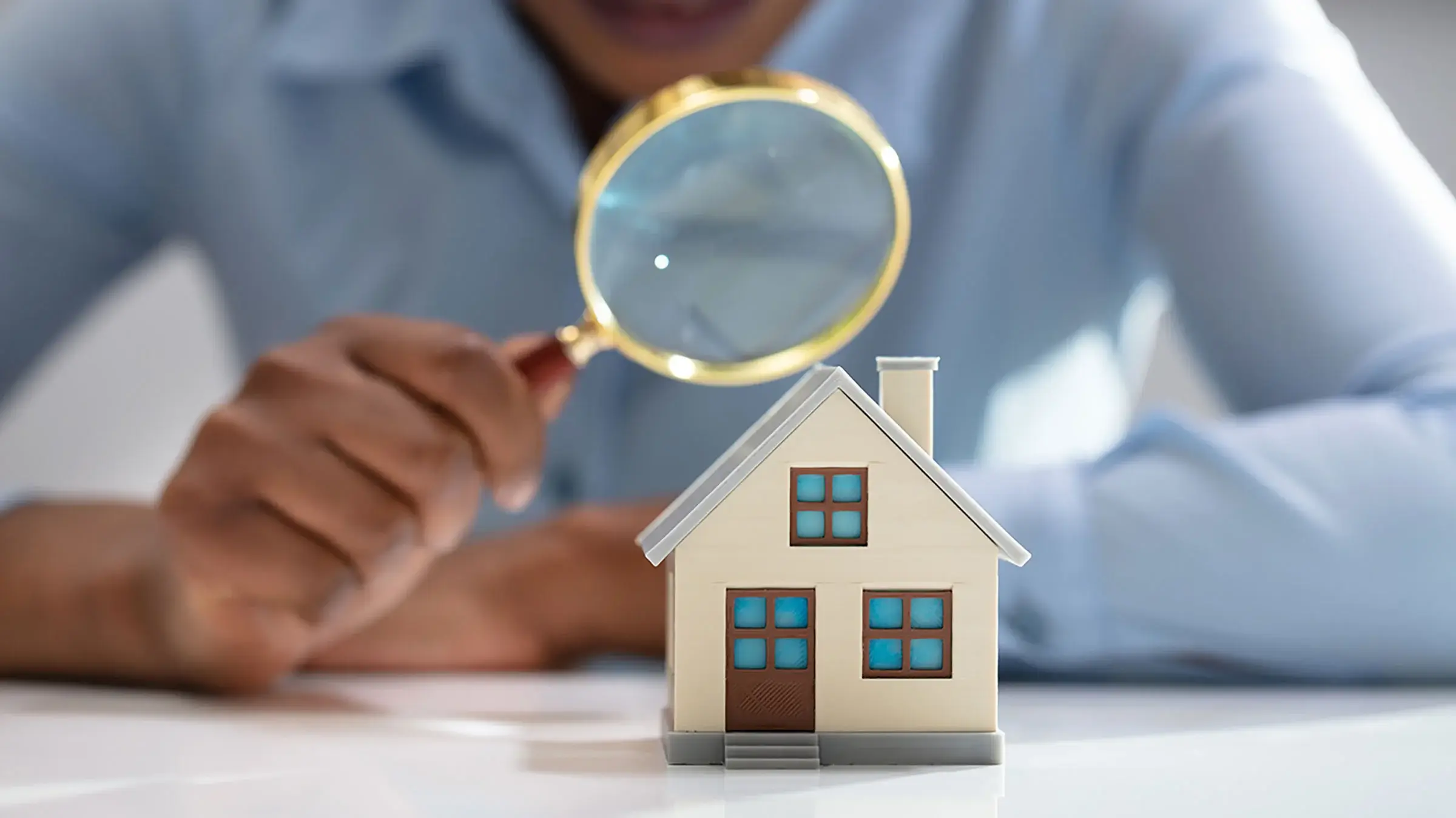 A person looking at a miniature house through a microscope.