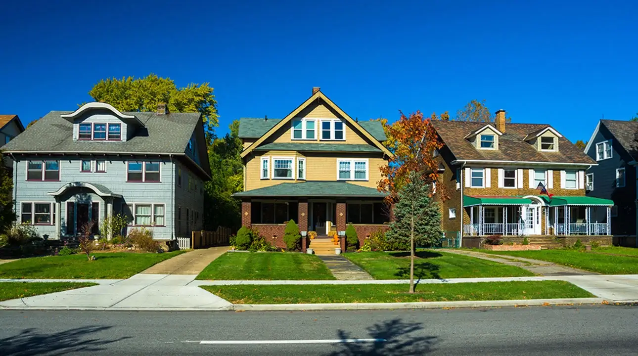 Three different-looking houses in a subdivision with green lawns, sidewalk and road in front.