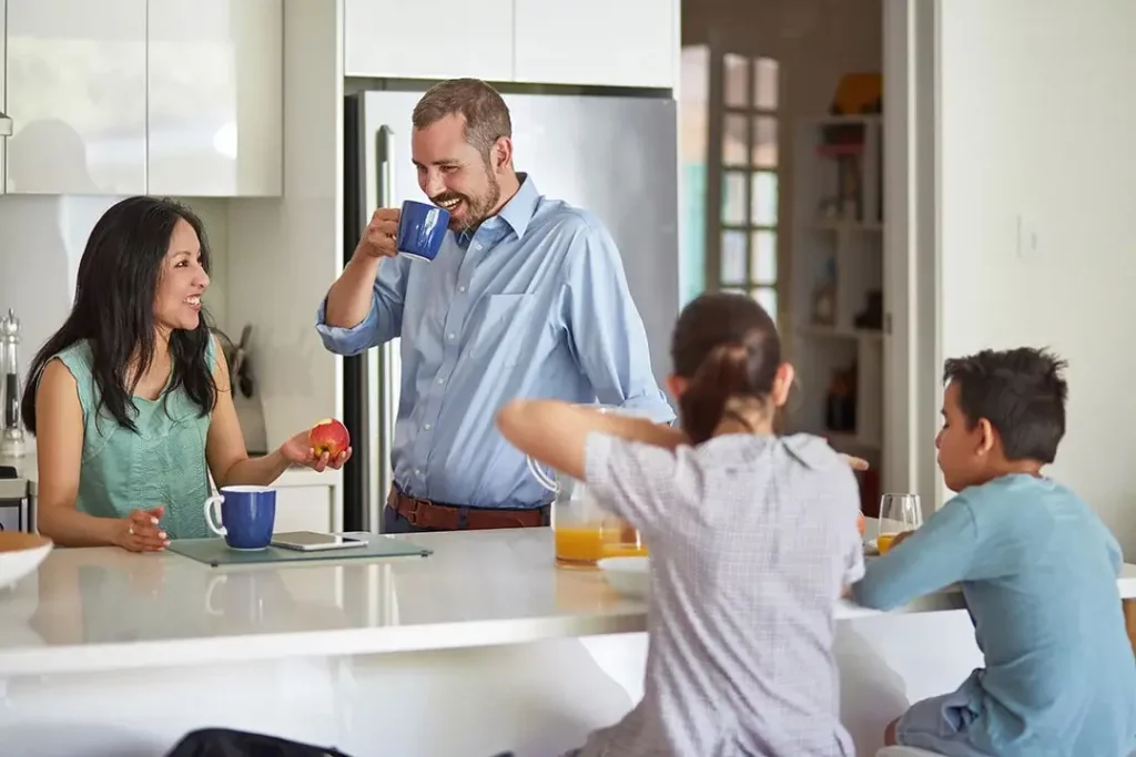 Two parents and two kids at kitchen counter in the morning drinking coffee and orange juice.