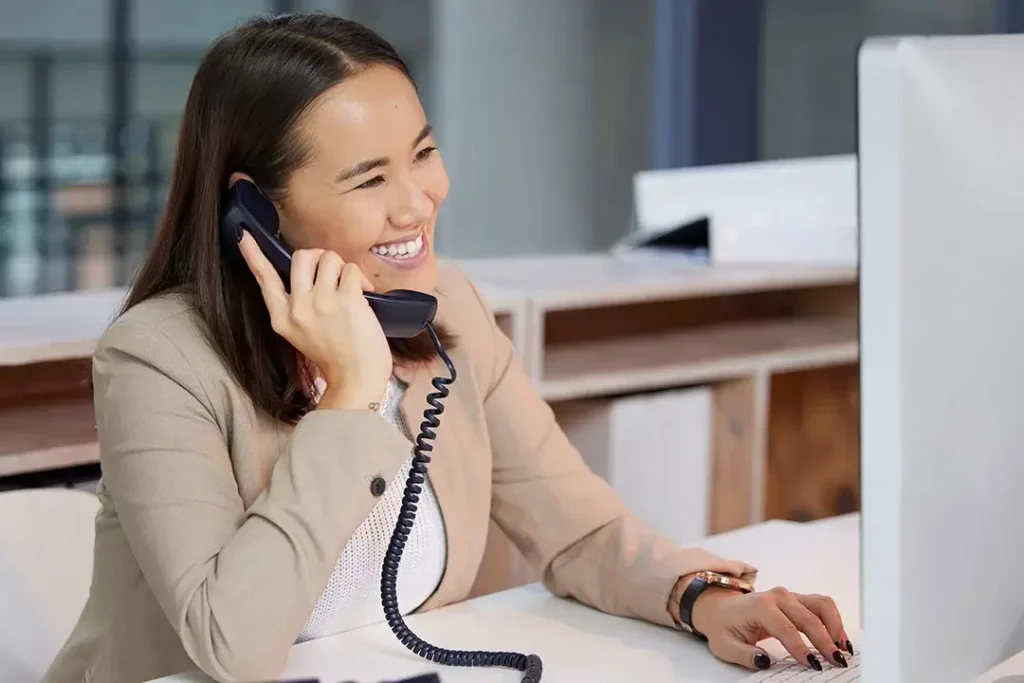 A businessperson talking on a corded phone while working on computer.