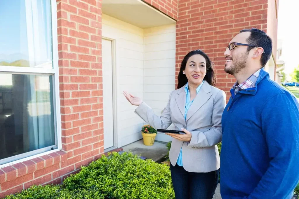 Businessperson holding tablet and gesturing towards house while talking with
consumer.