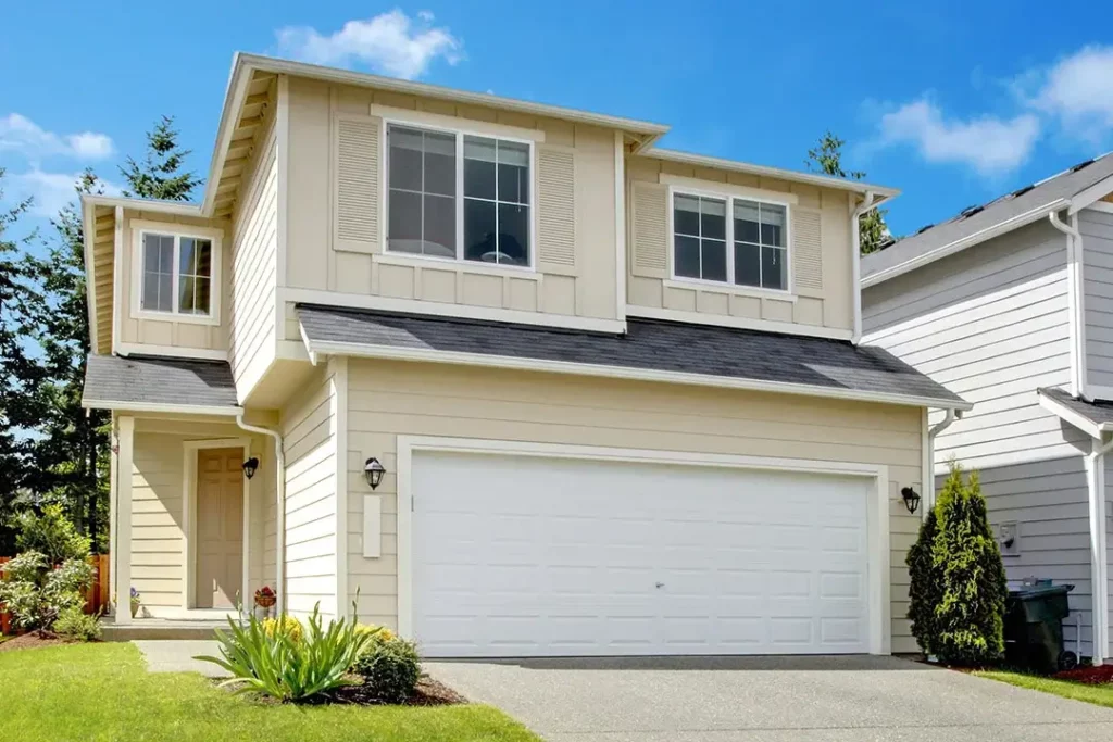 A cream-colored suburb house with a garage next to a gray house with a garage.