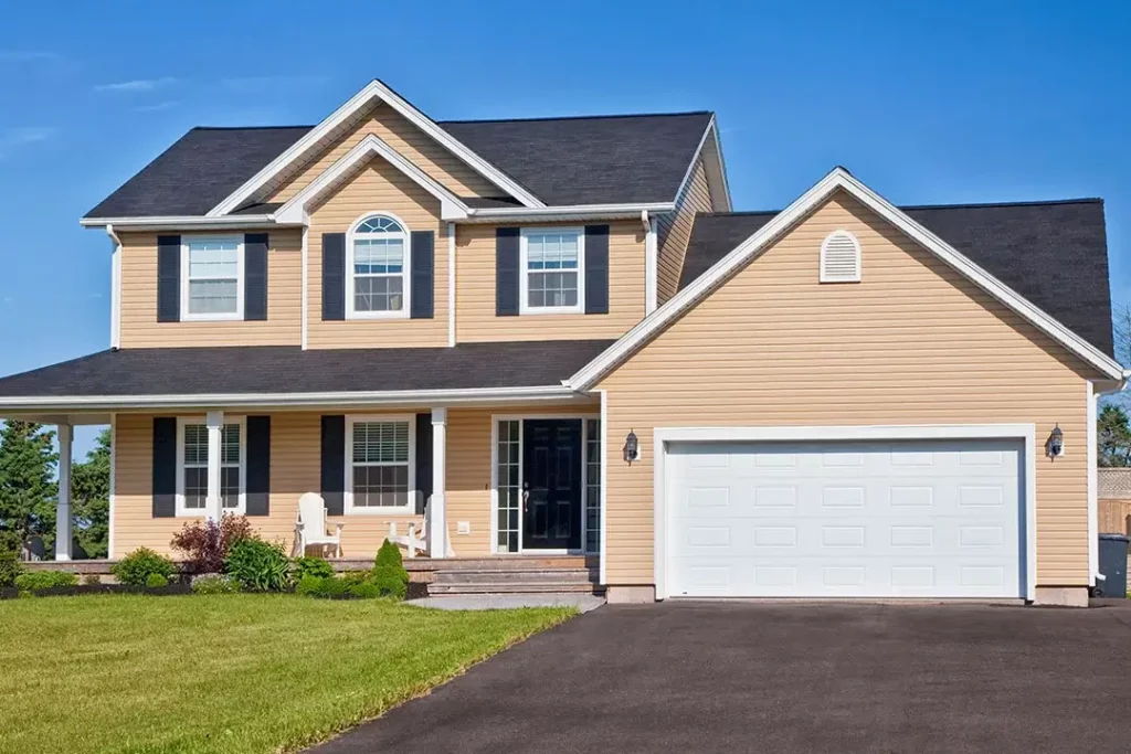 A beige house with a garage, green front lawn and paved driveway.