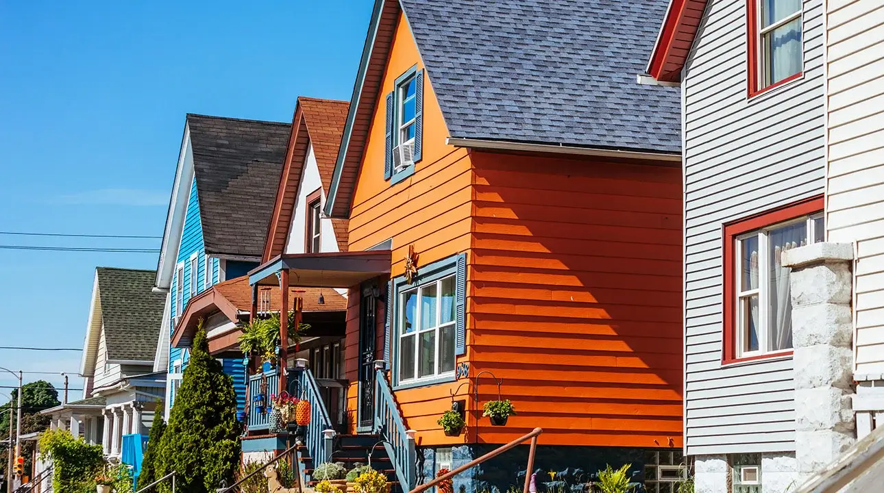 A row of white, orange and blue houses with flowers and shrubs outside.