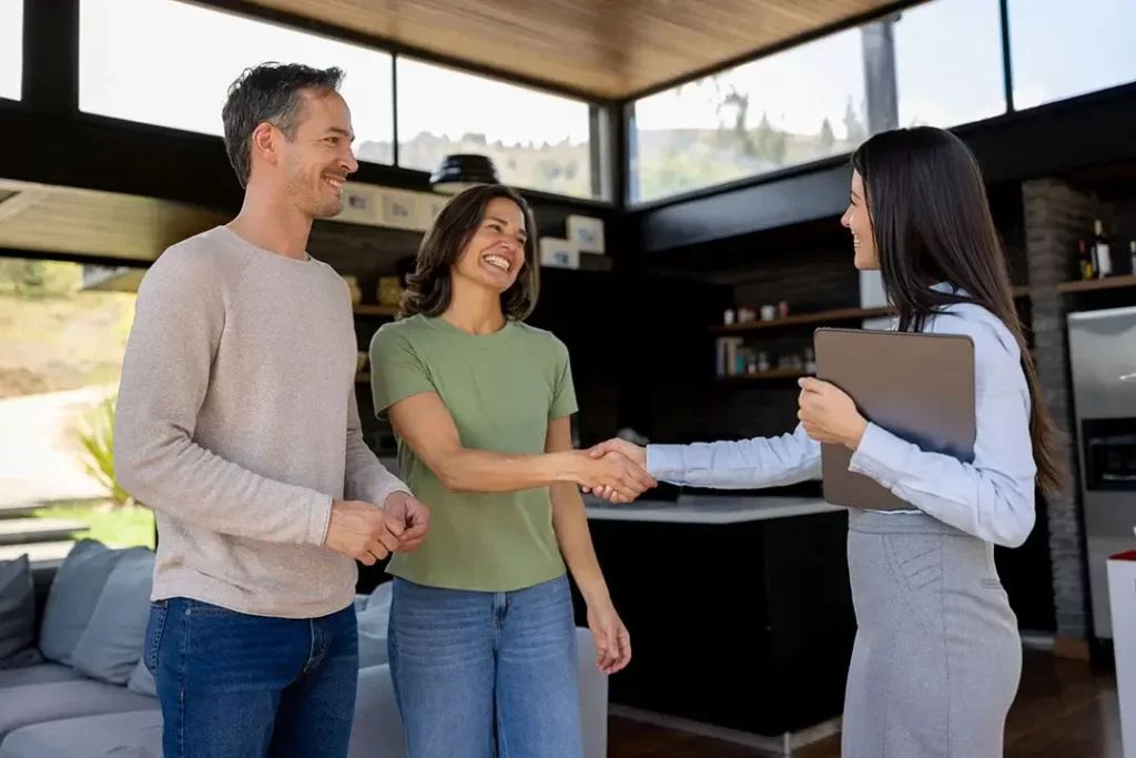 A couple smiling and shaking hands with a professionally dressed businessperson.