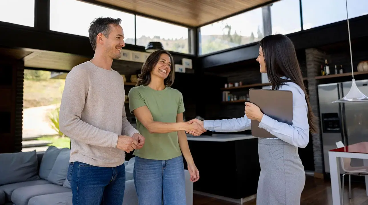 A couple smiling and shaking hands with a professionally dressed businessperson.