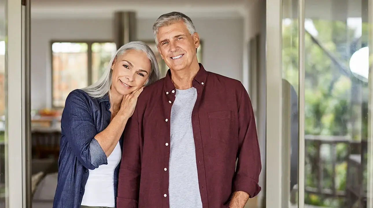 A middle-aged couple posing and smiling for camera while standing in glass doorway.