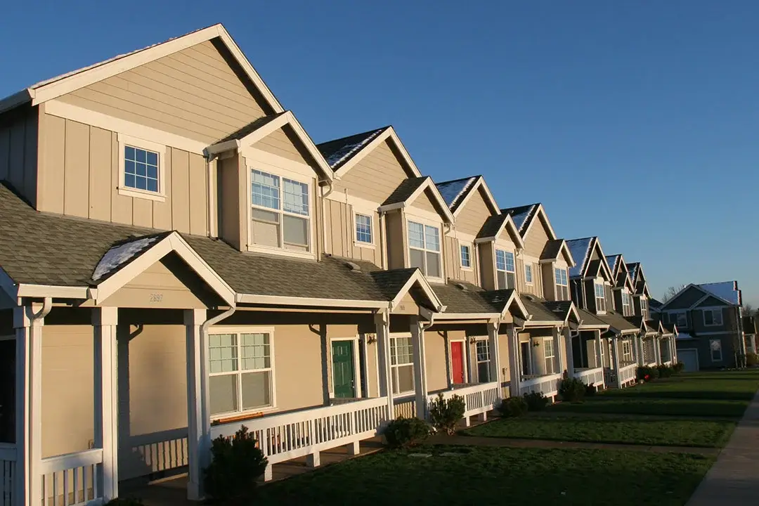 A row of houses in a subdivision at dusk, with green grass and a sidewalk in front.